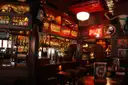 A warm pub interior with a long wooden bar, stools and a red neon sign