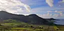 Green fields and dark hills by the sea on the Ring of Kerry under a cloudy blue sky