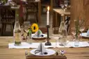 A rustic wooden dinner table with a lit candle, flowers and glasses