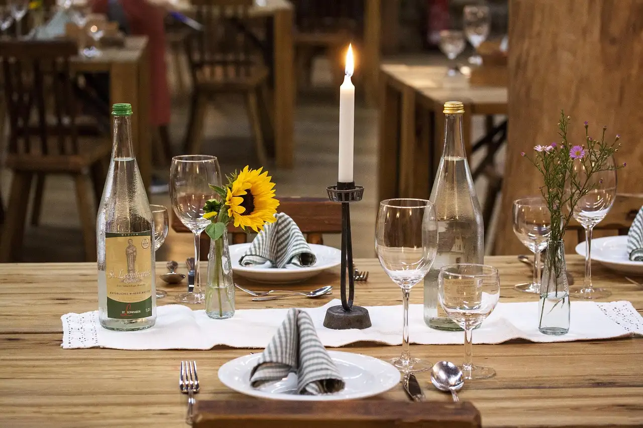 A rustic wooden dinner table with a lit candle, flowers and glasses