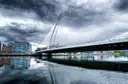 The white harp-shaped Samuel Beckett Bridge over the River Liffey under a stormy sky