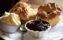 Scones with a bowl of jam and a bowl of cream on a plate