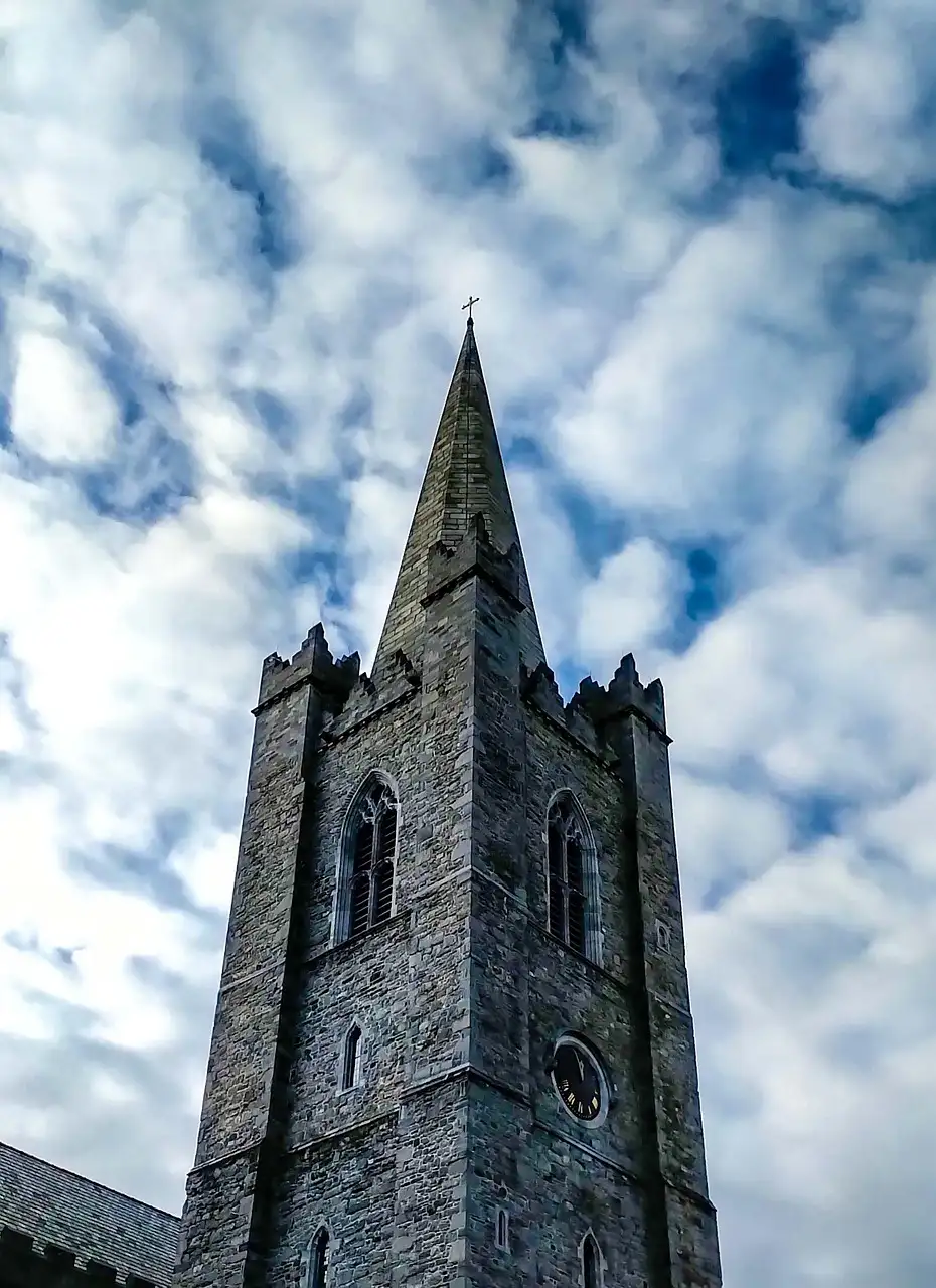 The grey stone tower and spire of St Patrick's Cathedral under a cloudy blue sky