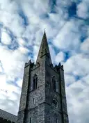 The grey stone tower and spire of St Patrick's Cathedral under a cloudy blue sky