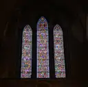 Three tall stained glass windows glowing in a dark stone wall