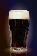 A pint of dark stout with a white head, lit against a dark background