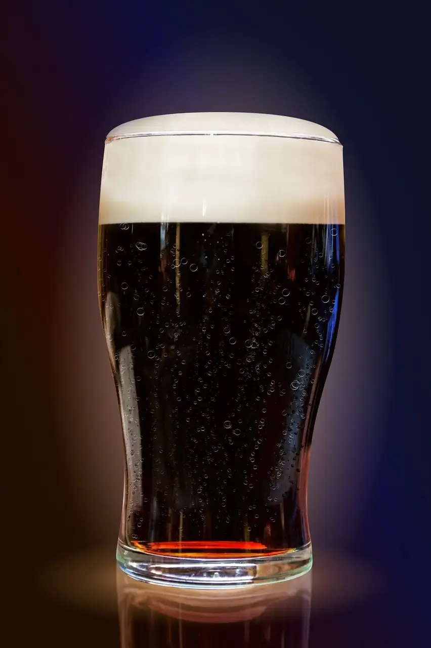 A pint of dark stout with a white head, lit against a dark background
