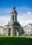 The stone bell tower in the main square of Trinity College Dublin, with a lawn in front and a blue sky