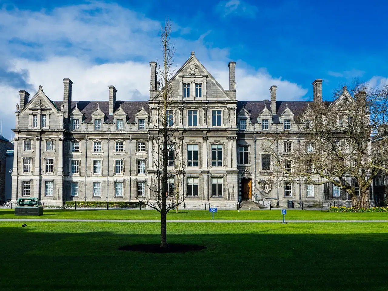 A grey stone college building behind a green lawn at Trinity College Dublin