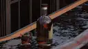 A bottle and a small glass of whiskey on a polished bar counter