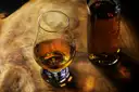 A glass of whiskey on a wooden board beside a bottle