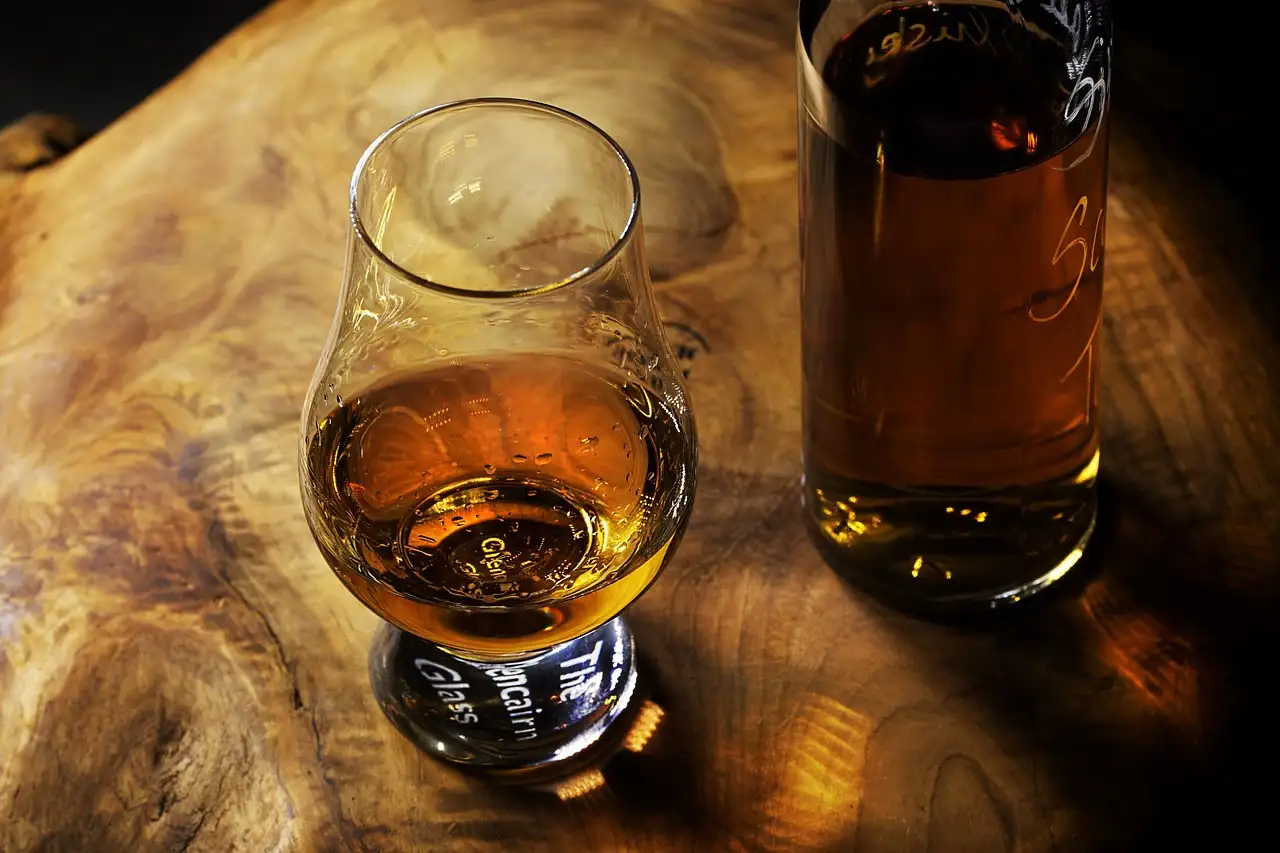 A glass of whiskey on a wooden board beside a bottle