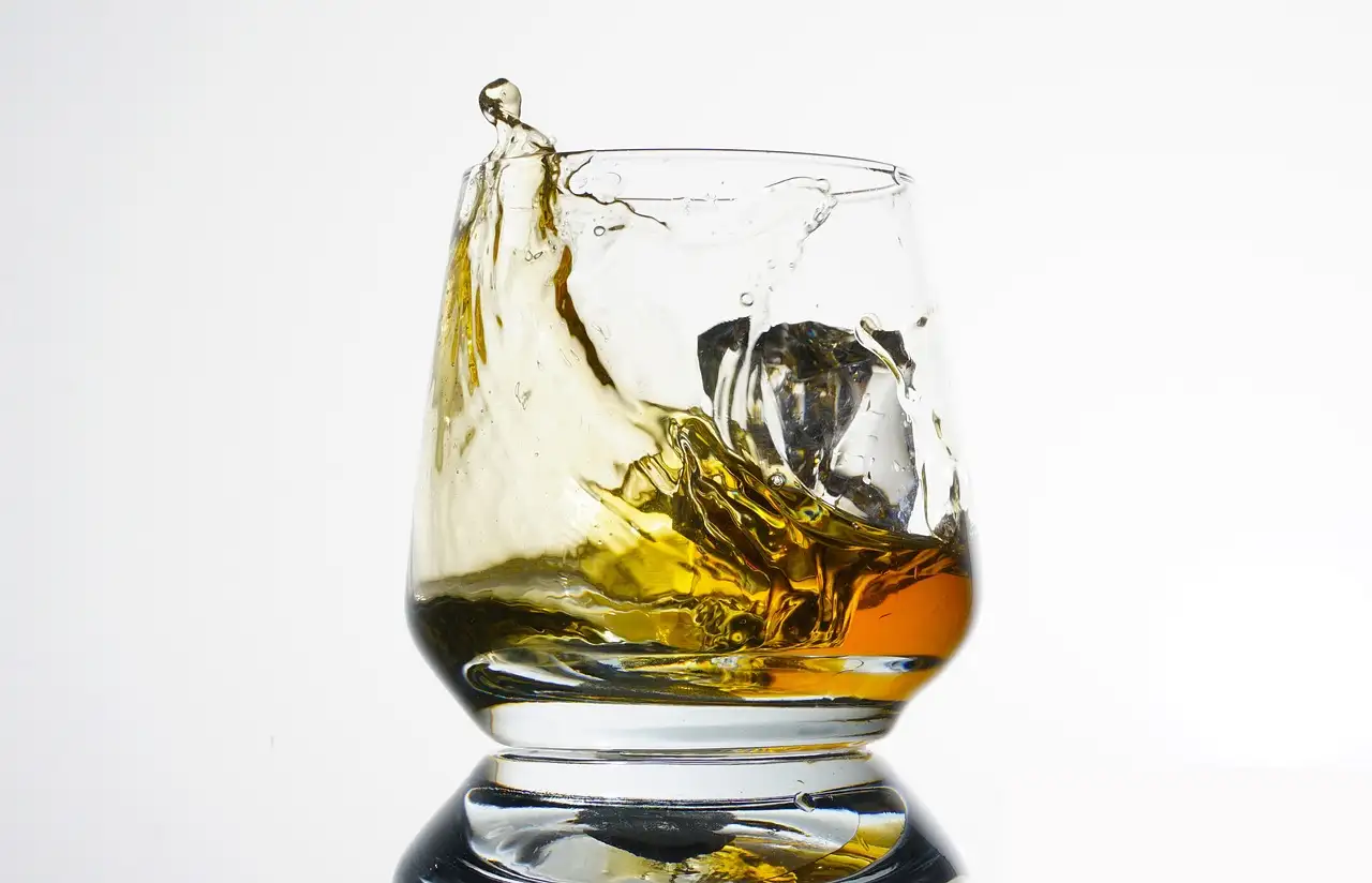 Whiskey swirling in a heavy glass tumbler on a white background